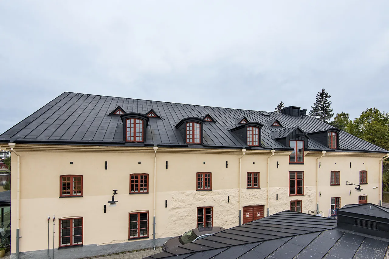 Ståendefalst tak i mörk plåt på putsad byggnad med takkupor